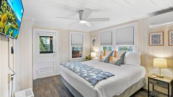 Une chambre à coucher avec un lit, un ventilateur de plafond, une télévision et une fenêtre avec des stores.