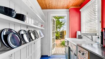 Une cuisine étroite avec des meubles blancs, un mur d’accent rouge et une vue sur le jardin.