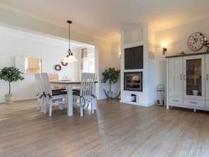 A dining area with a wooden table and chairs, a hanging light fixture, and a fireplace. - Apartment 90 in the Stella Guesthouse (St. Peter-Ording)