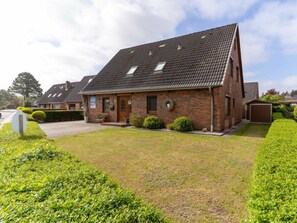 A two-story brick house with a sloped roof, a front porch, and a small garden. - Apartment 90 in the Stella Guesthouse (St. Peter-Ording)
