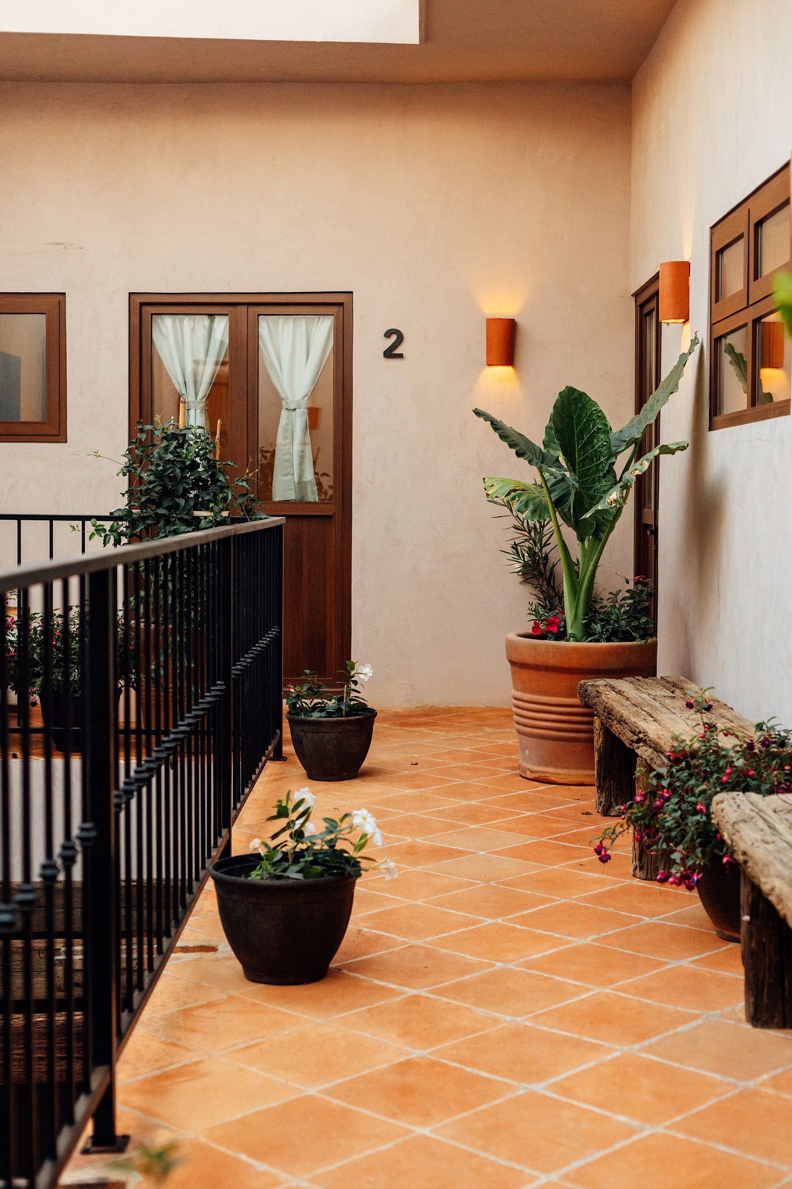 A corridor with a tiled floor, a wooden bench, potted plants, a staircase, and a wall-mounted number '2'.