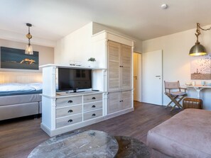 A modern bedroom with a bed, a TV, a wardrobe, and a dining area with a table and chairs. - Holiday Apartment With 1 Bedroom (St. Peter-Ording)