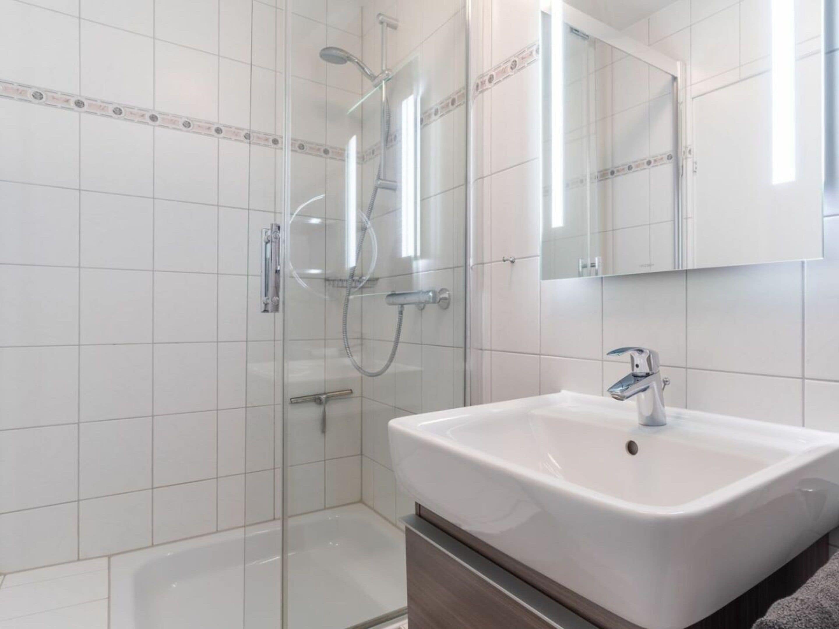 A modern bathroom with a glass-enclosed shower, a white sink, and a mirror above it.