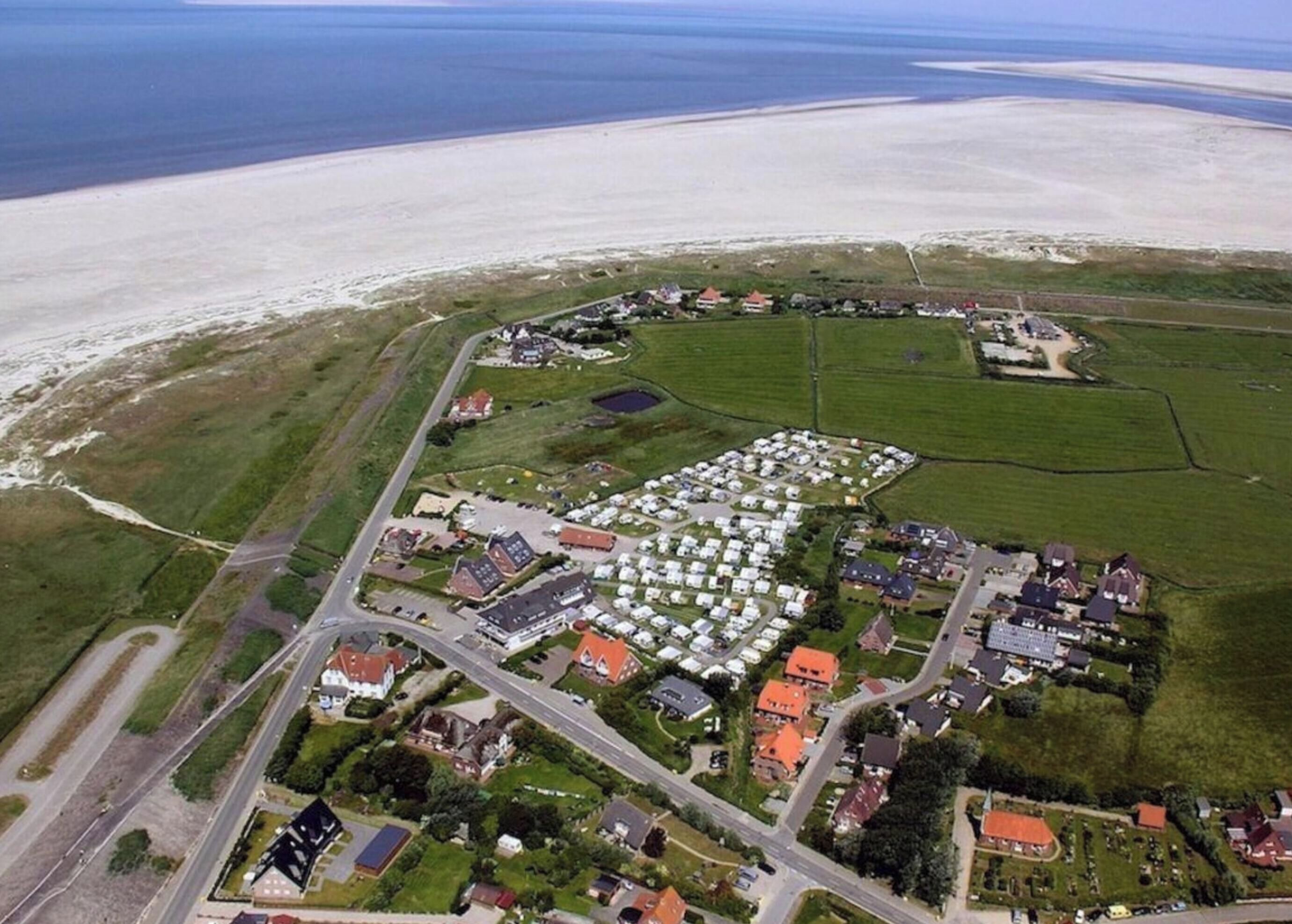 An aerial view of a coastal area with a large caravan park, several buildings, and a road network.