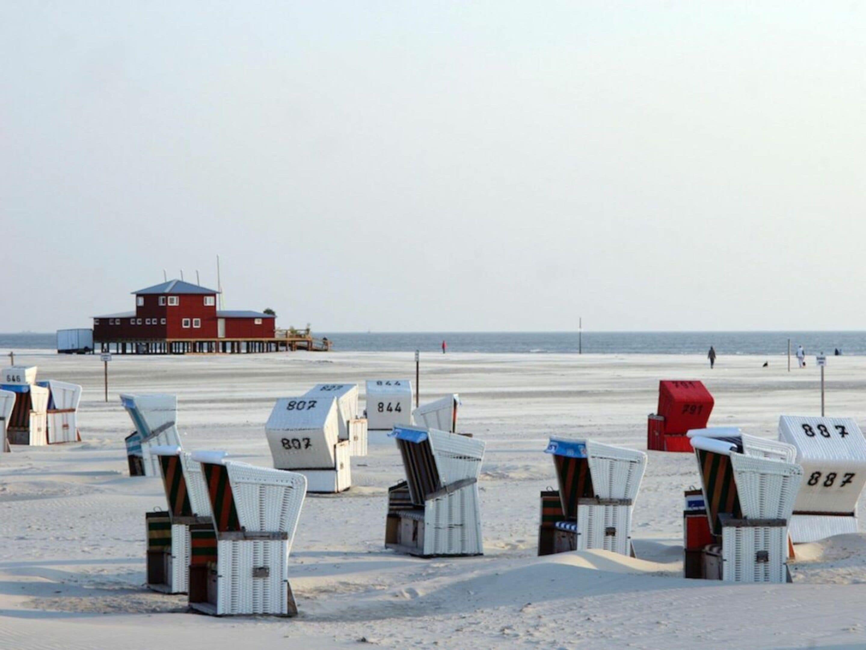 Sillas de playa con números, una torre de salvavidas y el océano al fondo.