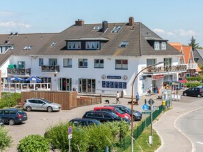 A two-story building with a restaurant on the ground floor and a shop on the upper level. There is a parking area in front with several cars. - Holiday Apartment With 1 Bedroom (St. Peter-Ording)
