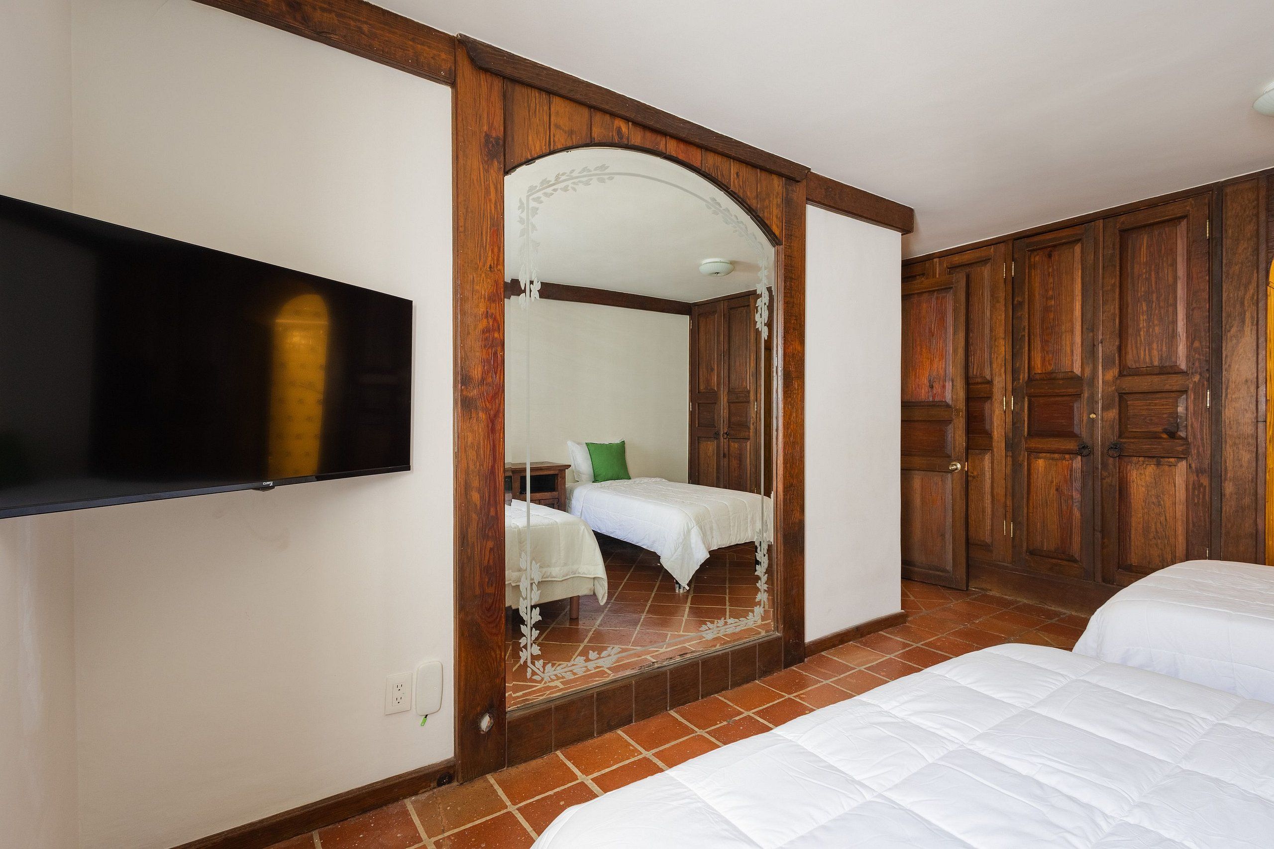 A hotel room with a large mirror, a bed, a television, and wooden wardrobes.