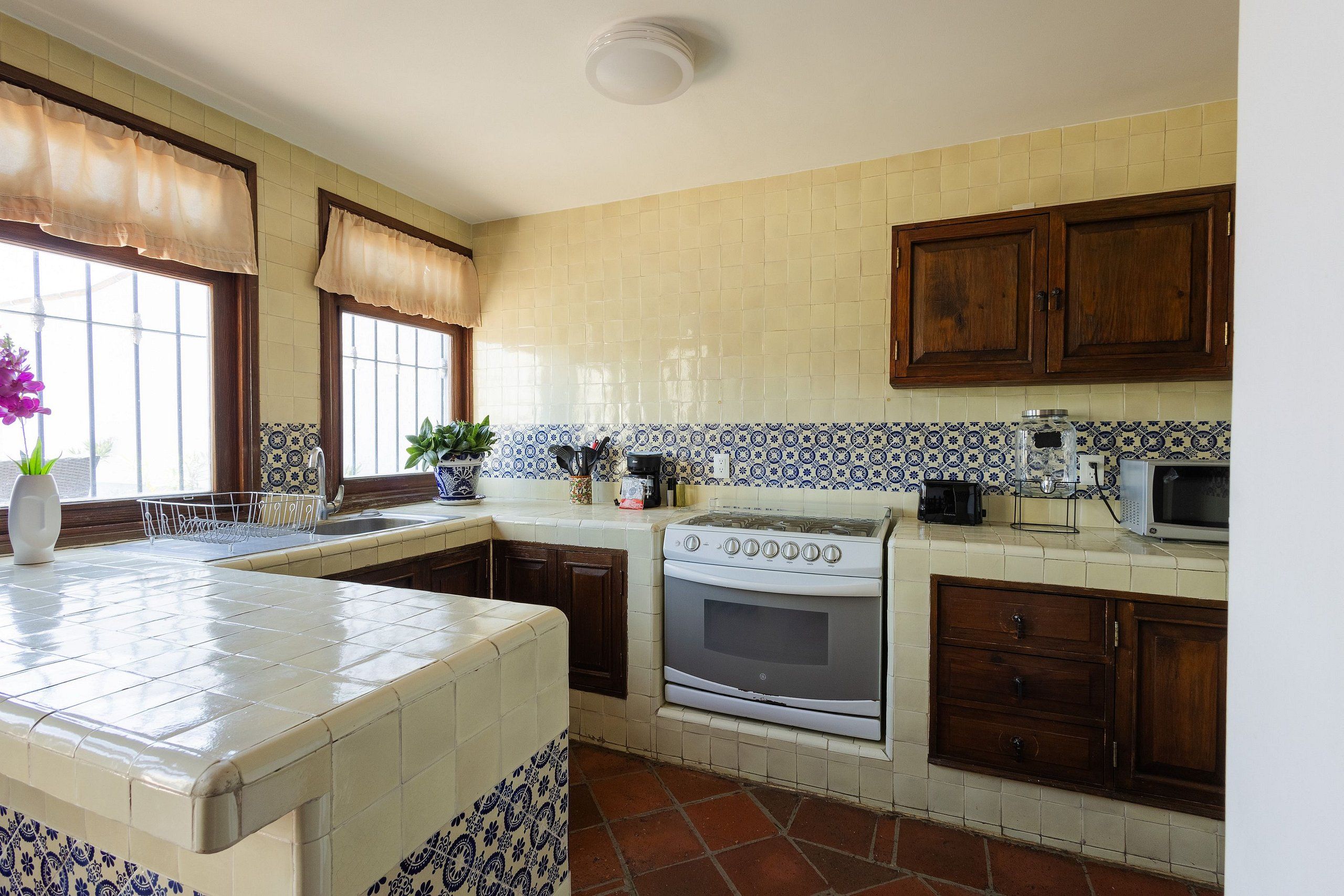A kitchen with a stove, oven, microwave, and a window with a curtain.