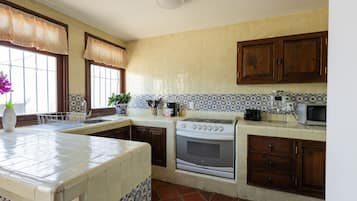 A kitchen with a stove, oven, microwave, and a window with a curtain.