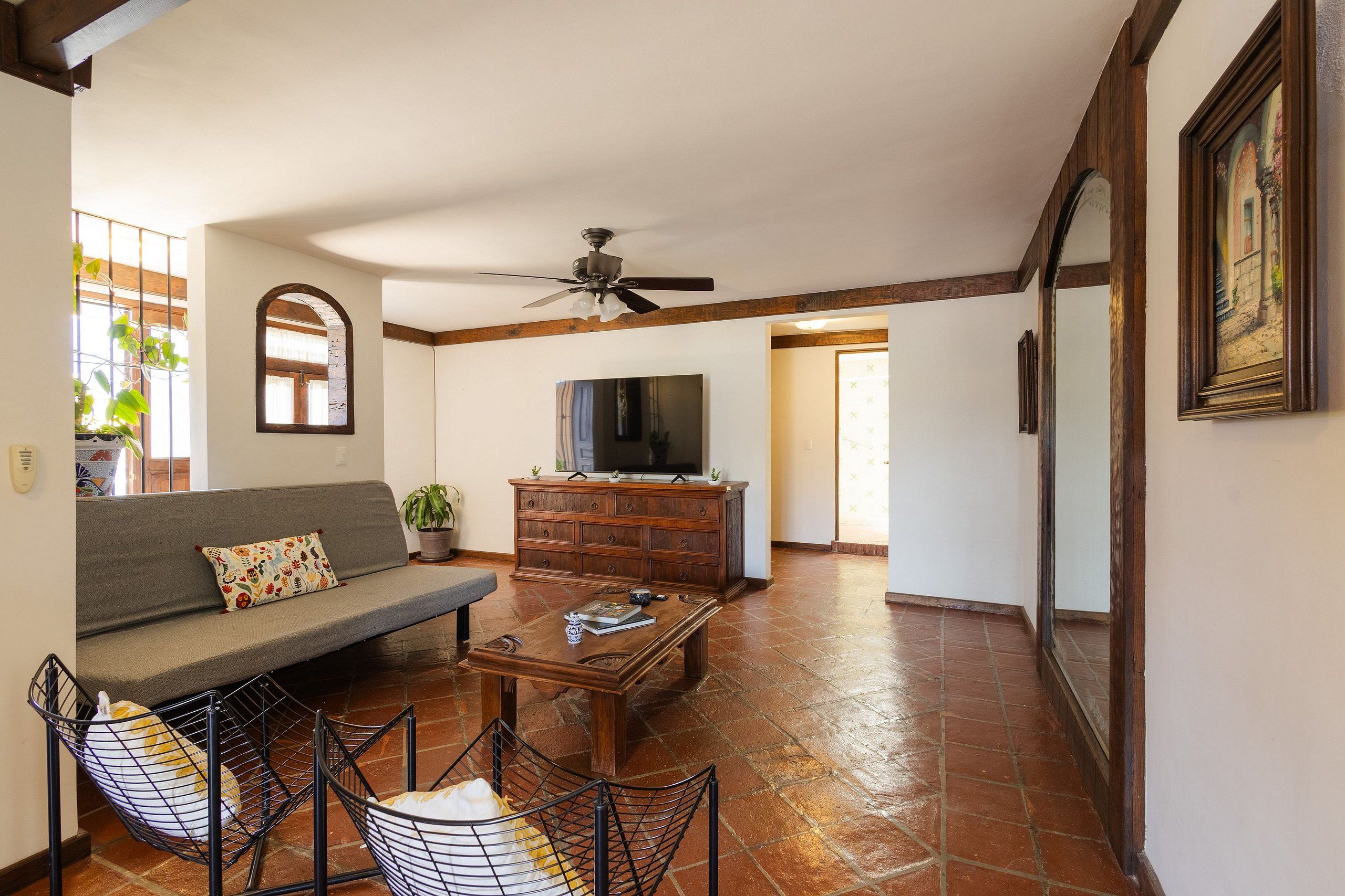 A living room with a sofa, coffee table, and chairs, a television, and a ceiling fan.