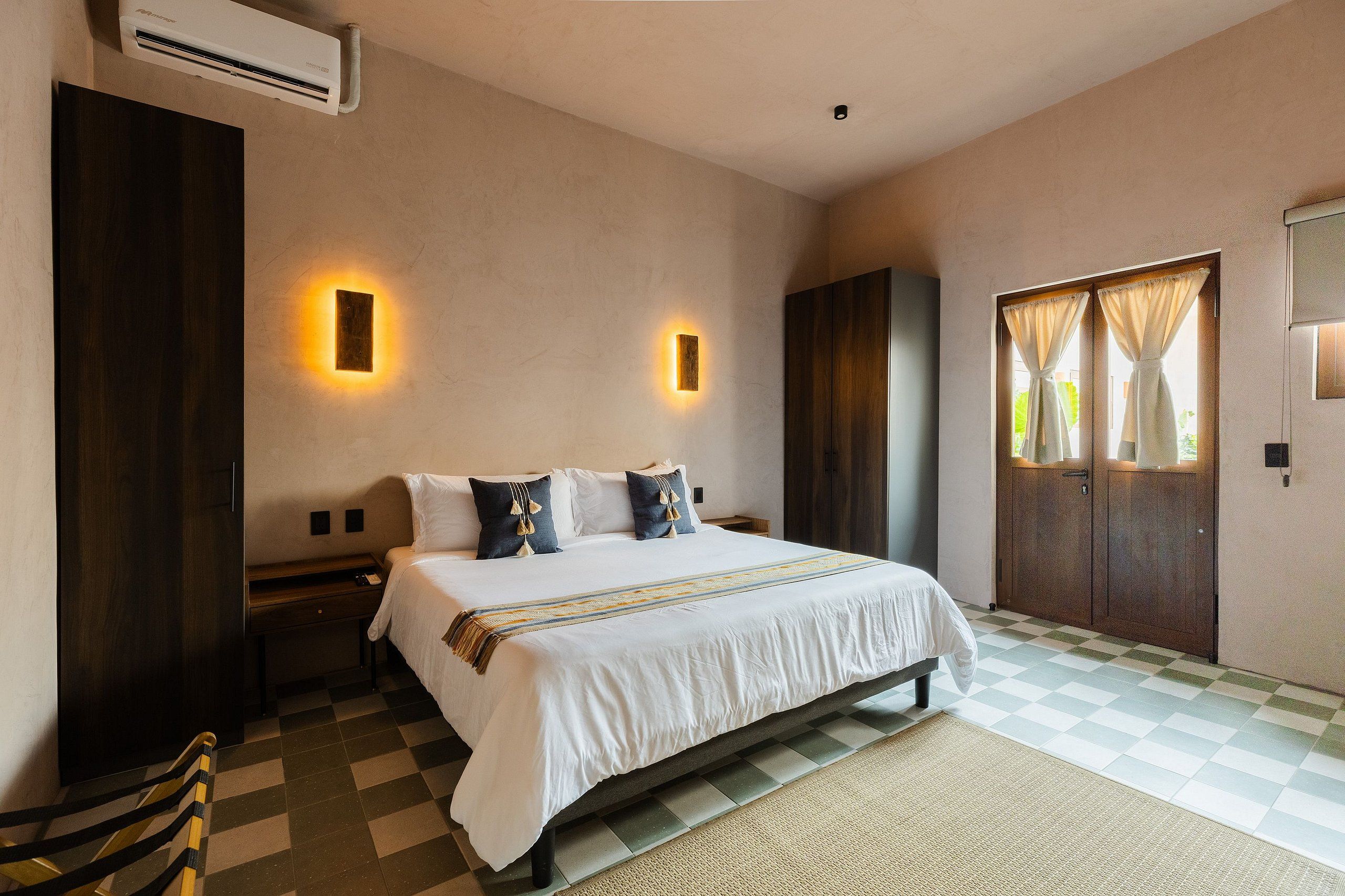 A hotel room with a large bed, two bedside tables, a wardrobe, and a window with curtains.