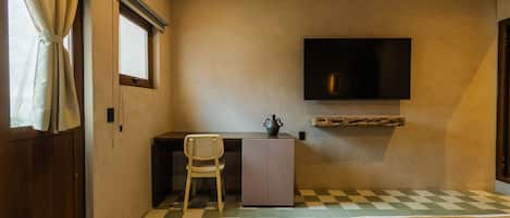 Una habitación con piso a cuadros, una cama, un escritorio con una silla, un televisor montado en la pared y un ventanal con cortinas.
