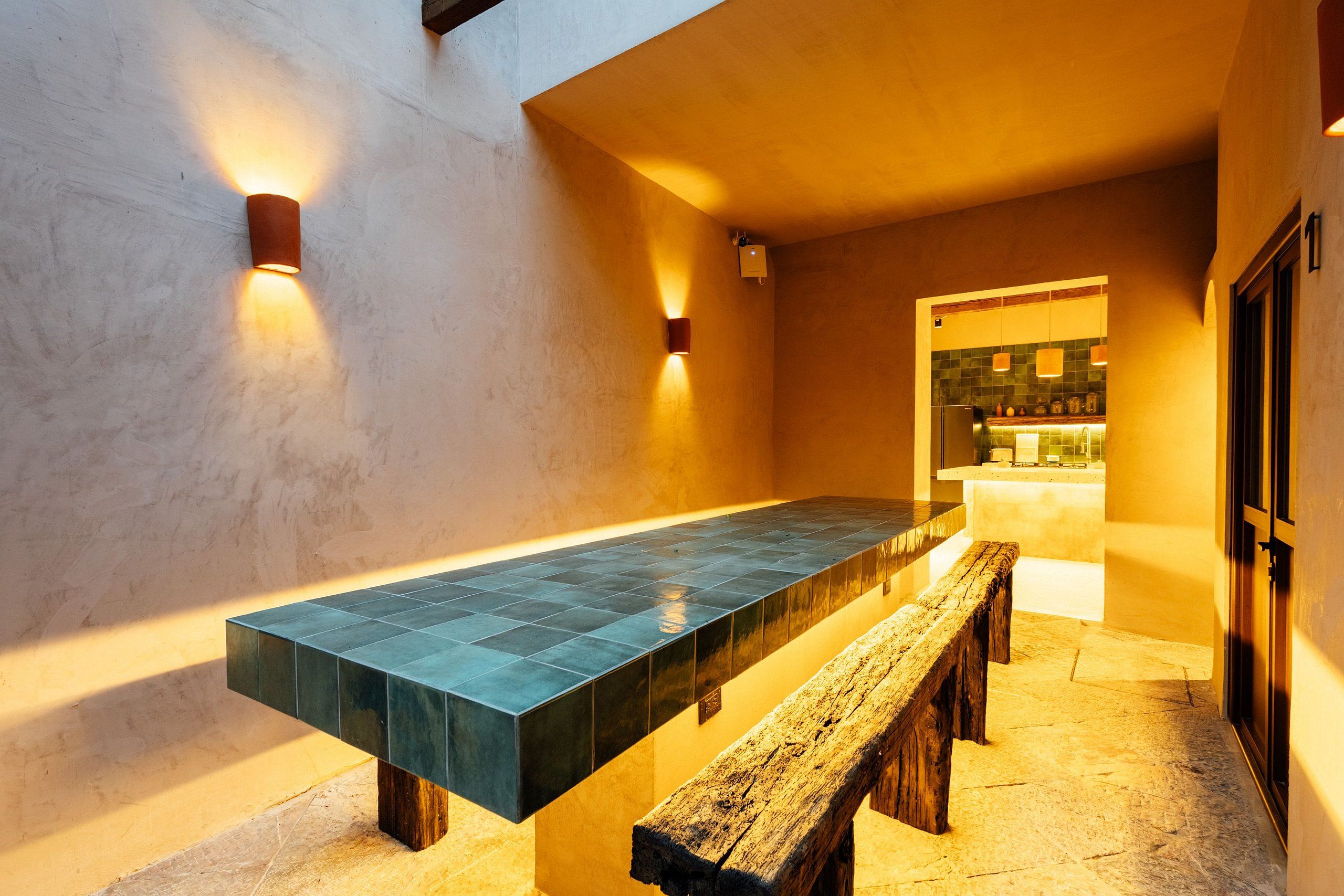 A long, rectangular table with benches on either end, set against a wall with two wall-mounted lights.