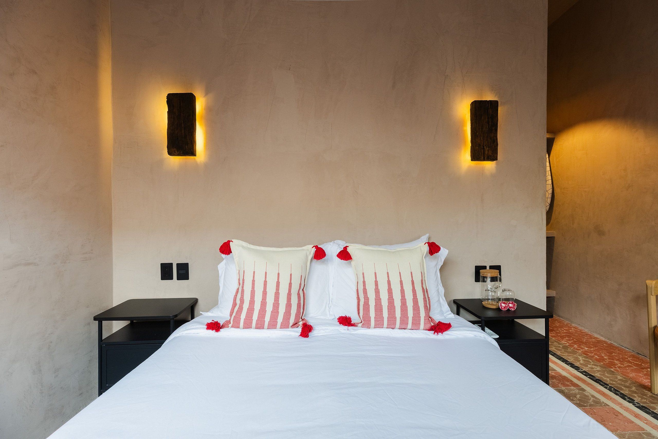 A hotel room with a large bed, two bedside tables, a nightstand, and a wall-mounted light fixture.
