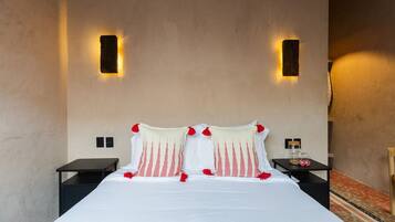A hotel room with a large bed, two bedside tables, a nightstand, and a wall-mounted light fixture.