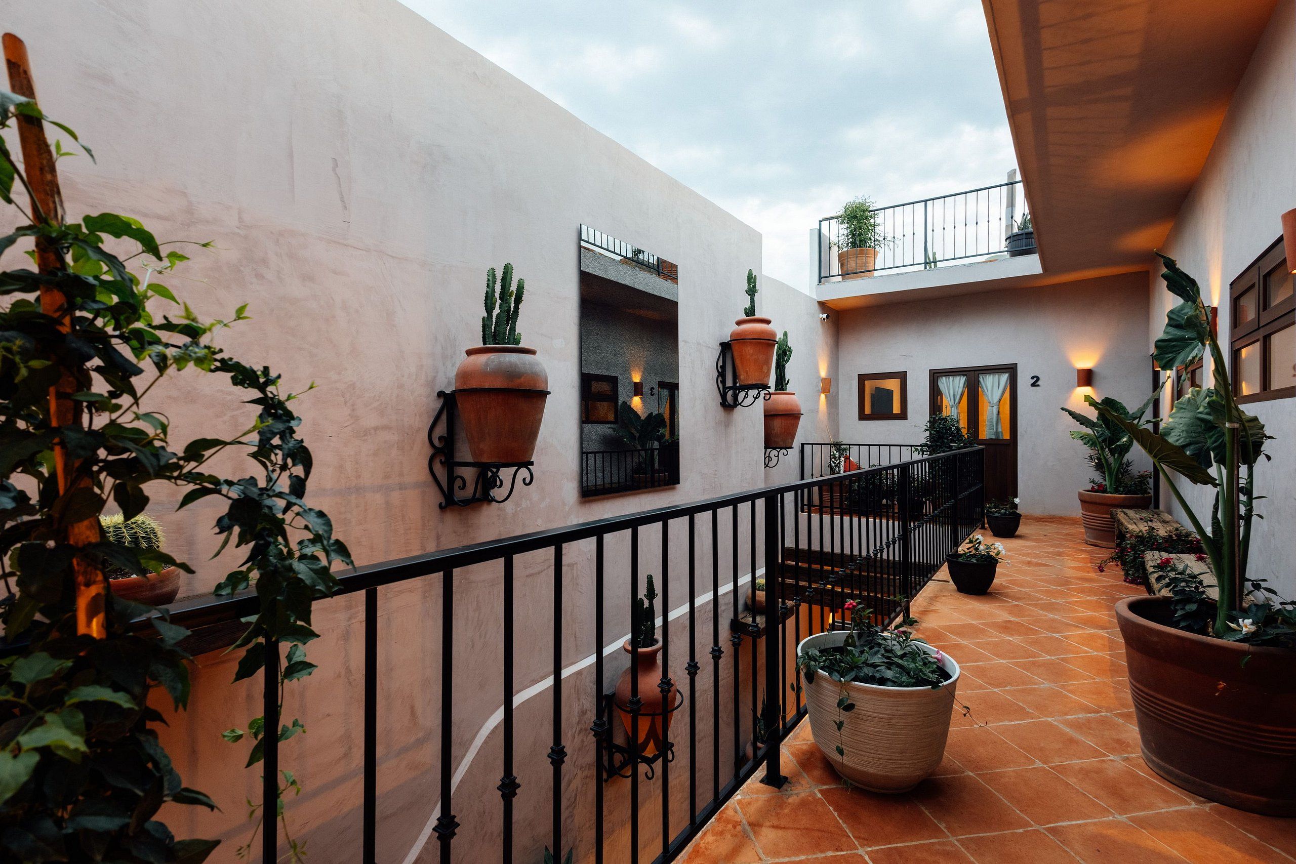 A courtyard with terracotta tiles, potted plants, and a black wrought iron railing.