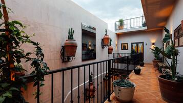 A courtyard with terracotta tiles, potted plants, and a black wrought iron railing.