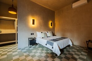 A hotel room with a checkered floor, a bed with white bedding and patterned pillows, a nightstand, a shelf with a lamp, and two wall-mounted light fixtures. - Boutique Loft Zenit | Air Conditioning and Rooftop (Puebla)