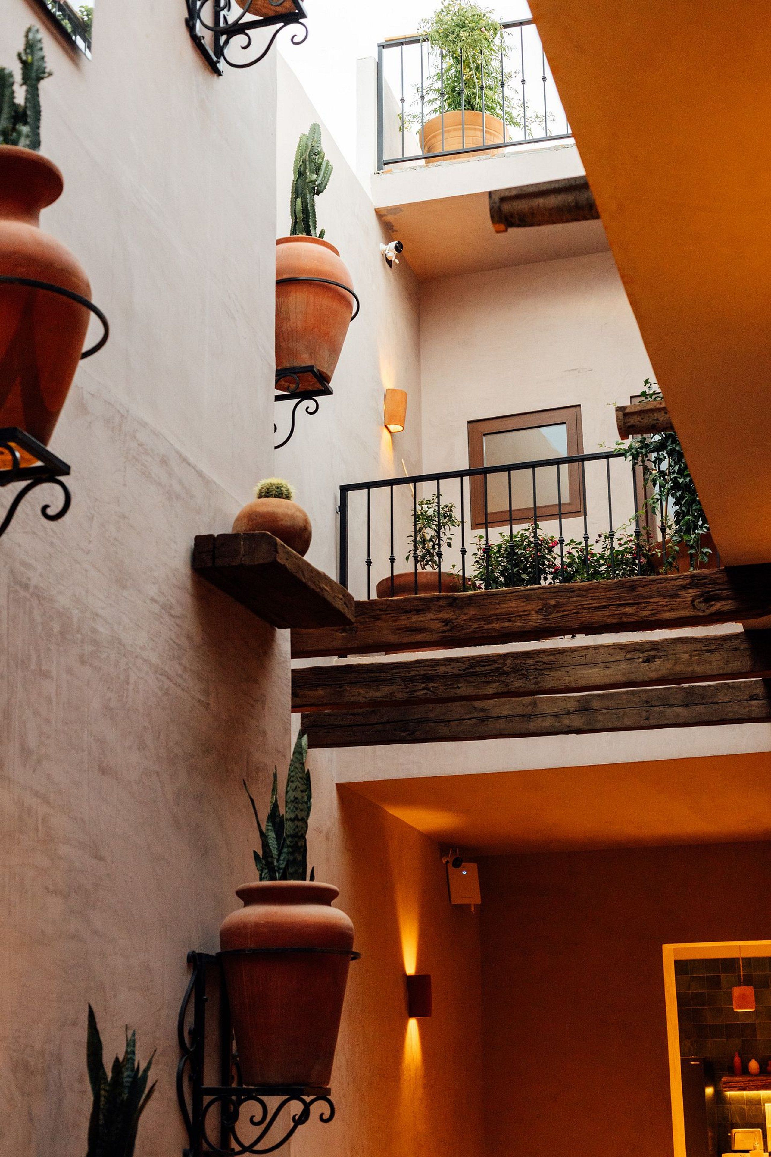 A multi-level interior with terracotta planters, a wooden staircase, and a balcony with a potted plant.