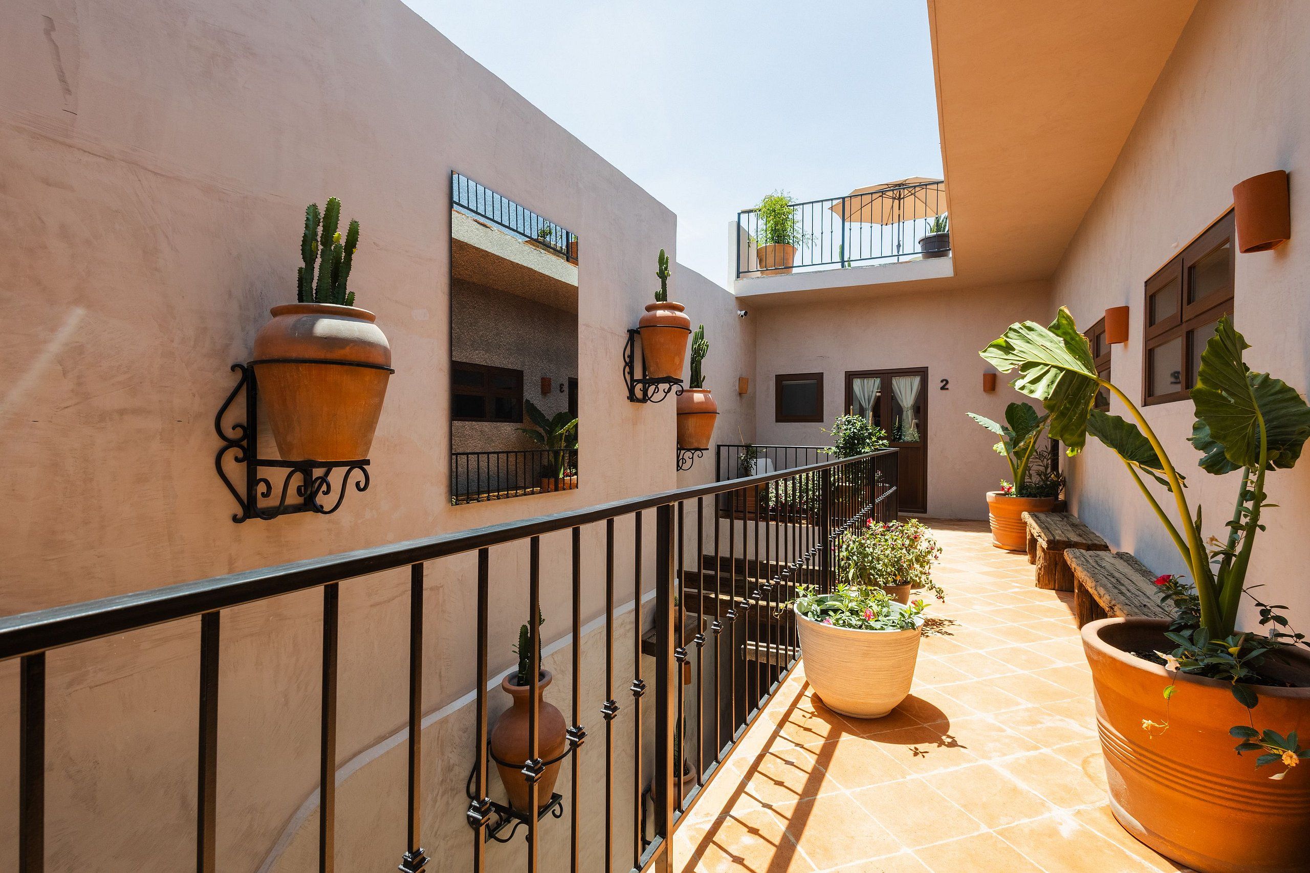 Un patio soleado con macetas de terracota, una barandilla metálica y una escalera que conduce a un nivel superior.