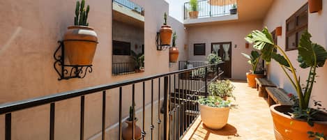 Un patio soleado con macetas de terracota, una barandilla metálica y una escalera que conduce a un nivel superior.