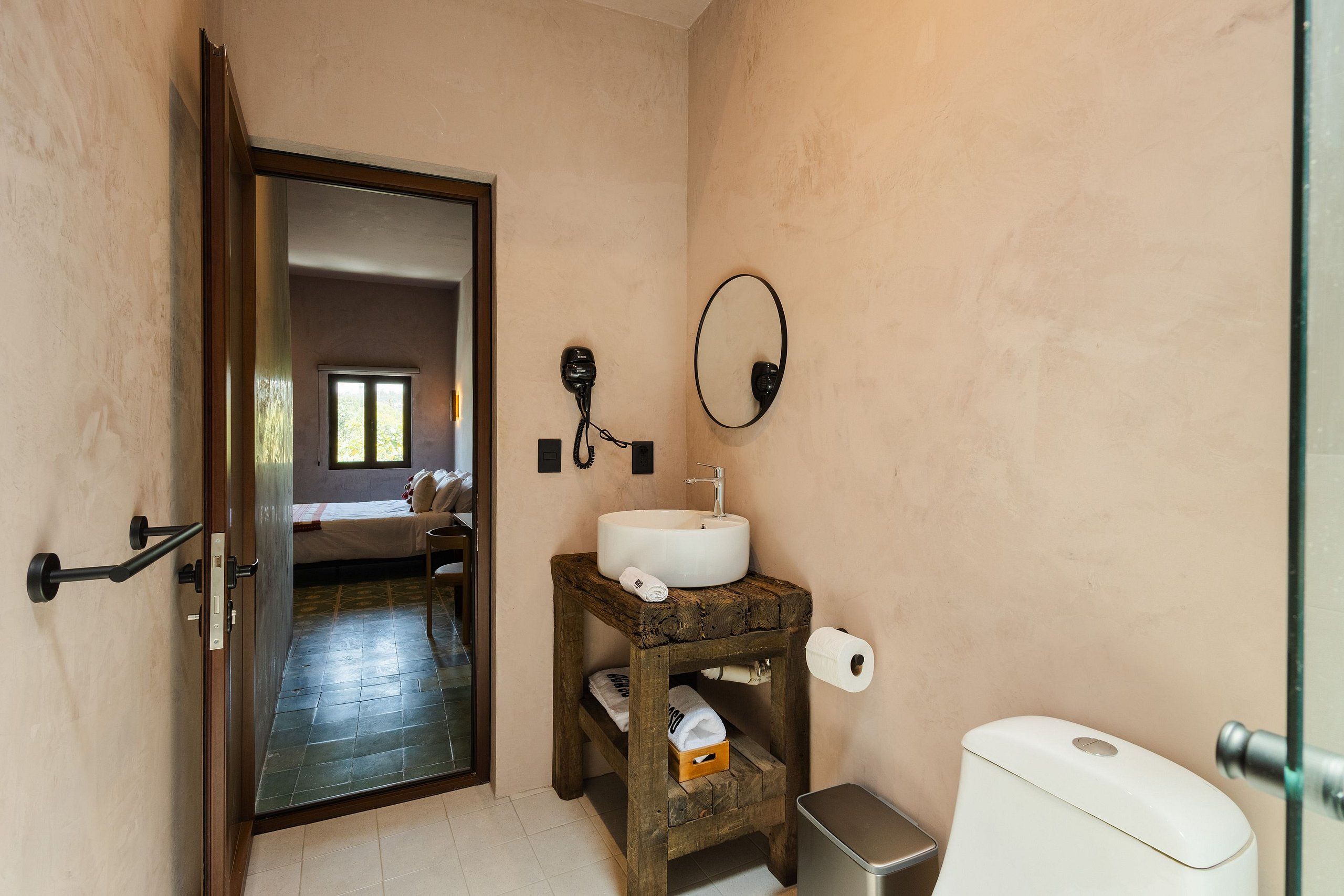 Un baño con inodoro, lavamanos, espejo y un taburete de madera.