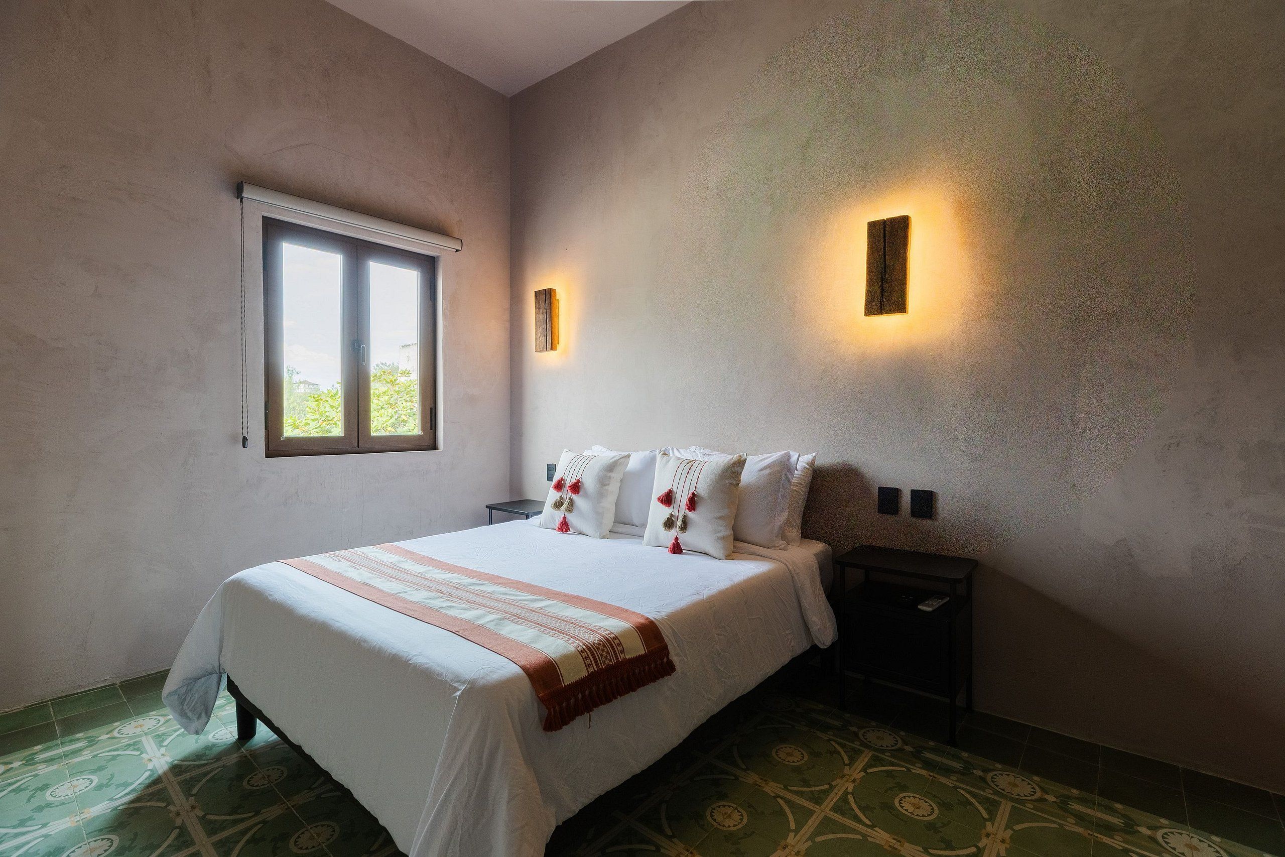 A bedroom with a bed, a nightstand, a window, and two wall-mounted lights.