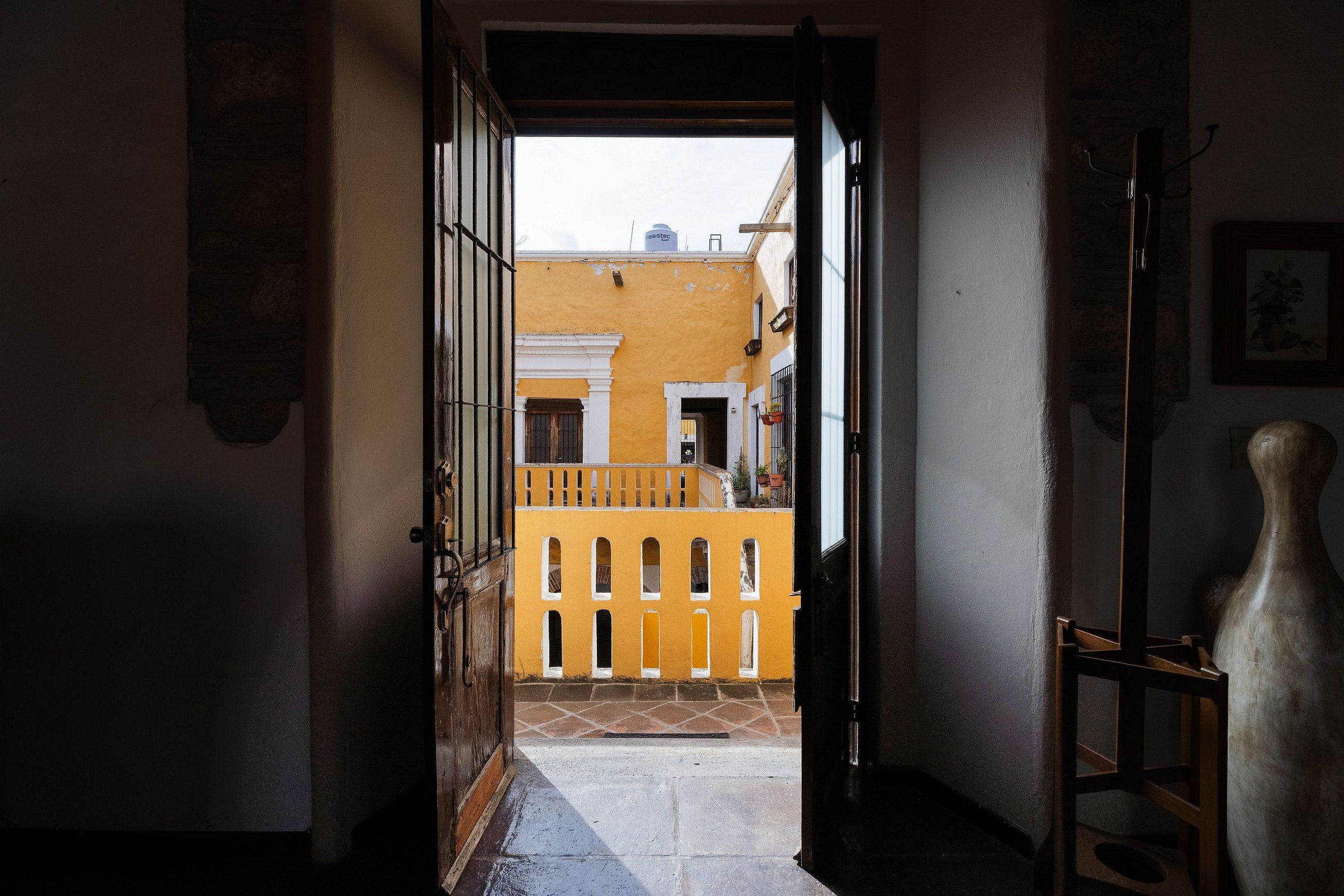 An open doorway leading to a courtyard with a yellow building, a wooden chair, and a potted plant.