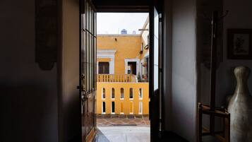 An open doorway leading to a courtyard with a yellow building, a wooden chair, and a potted plant.