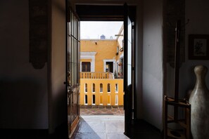 An open doorway leading to a courtyard with a yellow building, a wooden chair, and a potted plant. - Casa La Virgen | Washing machine + Parking (Heroica Puebla de Zaragoza)