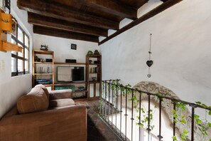 A living room with a sofa, television, wooden shelves, and a stone wall.