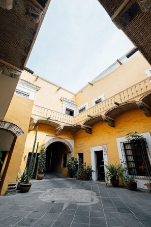 A courtyard with a yellow building, arched doorways, and potted plants. - Casa La Virgen | Washing machine + Parking (Heroica Puebla de Zaragoza)