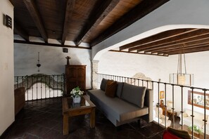 A cozy room with a wooden ceiling, a stone wall, a sofa, a table with a vase of flowers, and a hanging light fixture.