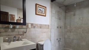 Une salle de bain avec des toilettes, un lavabo et une douche. Des tableaux encadrés ornent le mur.