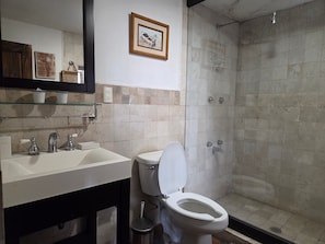 A bathroom with a toilet, sink, and shower. There are framed pictures on the wall. - Casa La Virgen | Washing machine + Parking (Heroica Puebla de Zaragoza)