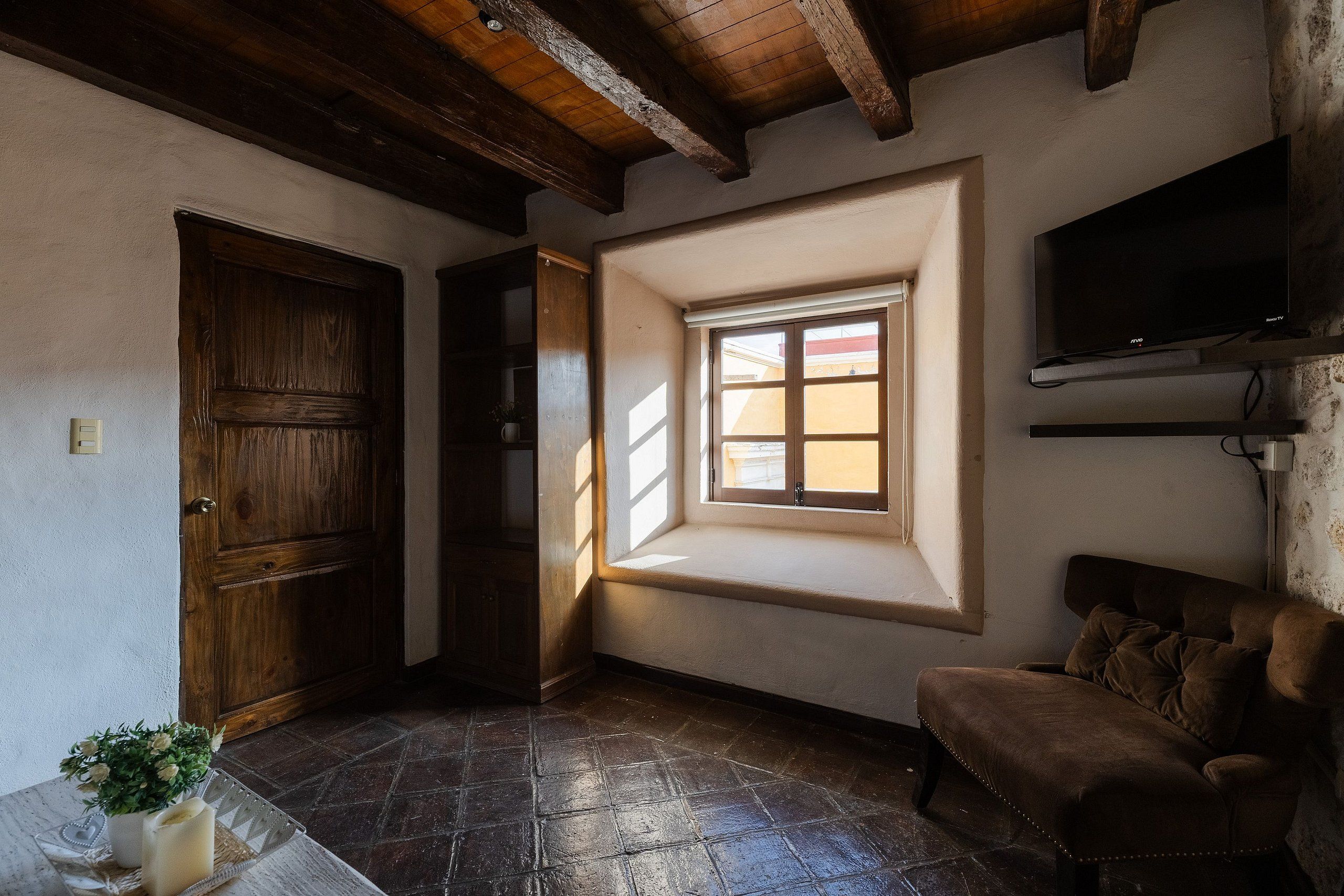 Une pièce avec une porte en bois, une fenêtre donnant sur un beau paysage, un canapé marron et un téléviseur fixé au mur.