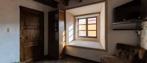 Una habitación con puerta de madera, ventana con vistas, sofá marrón y televisor en la pared.