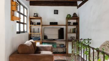 A cozy living room with a brown sofa, wooden shelves, a television, and a staircase with ivy.