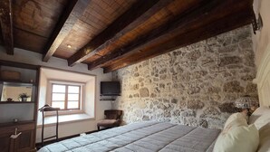 Une chambre avec un mur en pierre, un lit avec une literie blanche, un plafond en bois et une fenêtre.