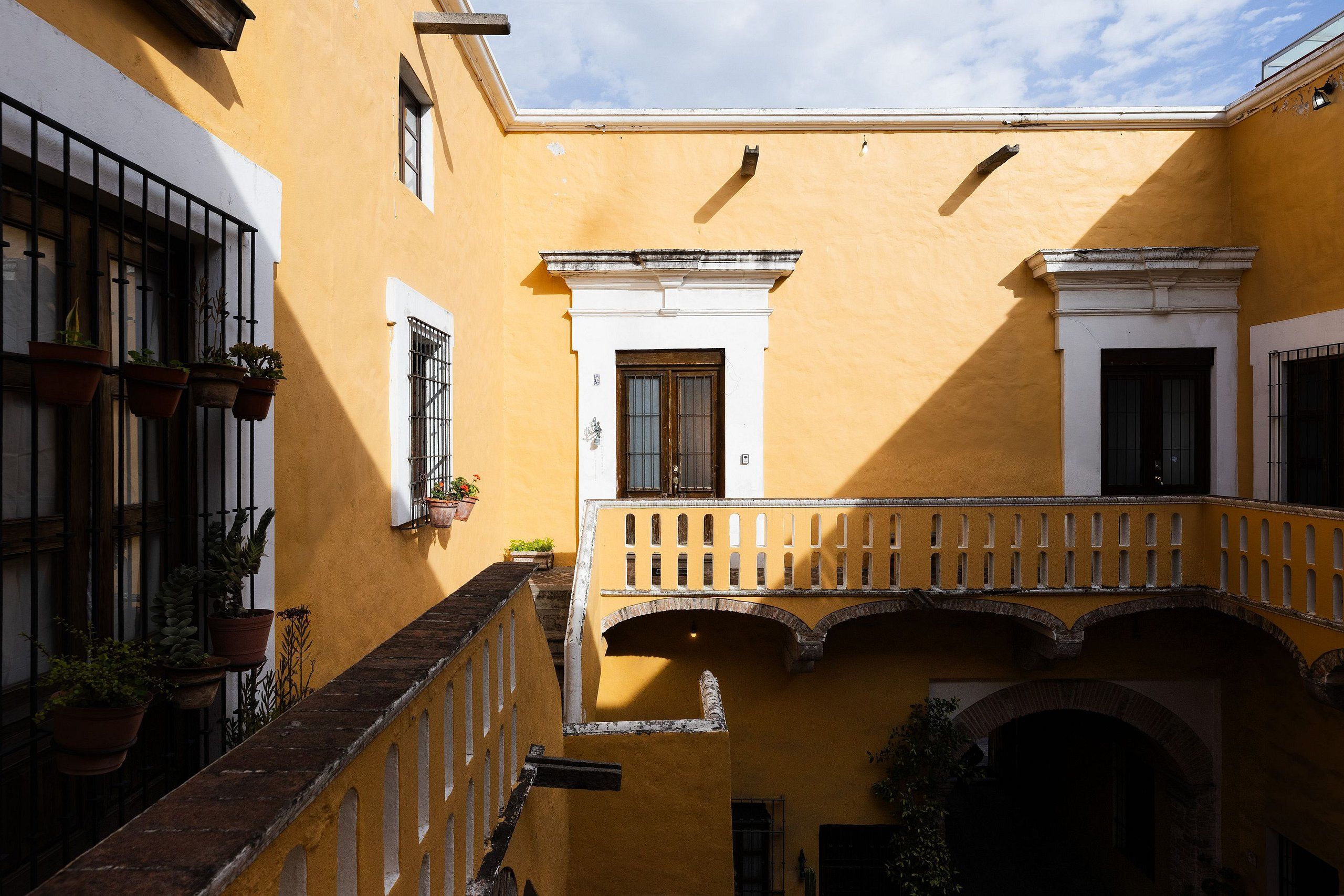 A courtyard with a yellow building, a white door, and a balcony with a railing.