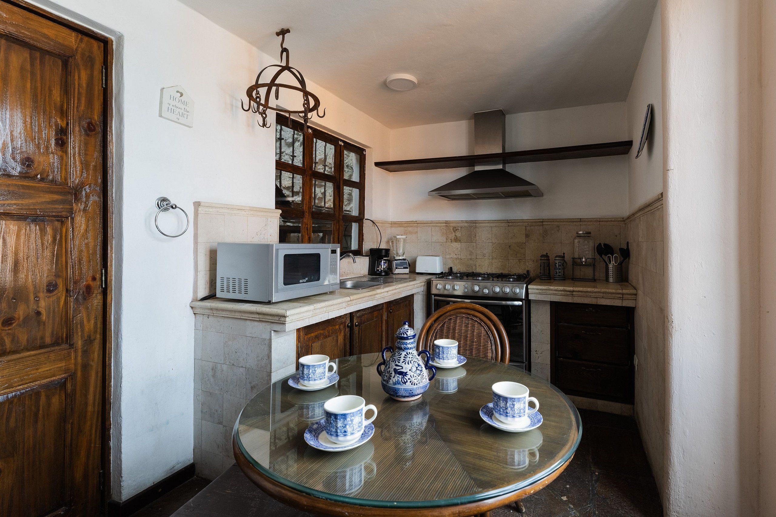 Una cocina compacta con una mesa redonda de vidrio dispuesta para tomar té, un microondas, una estufa y una lámpara colgante.