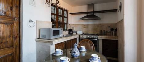 Una cocina compacta con una mesa redonda de vidrio dispuesta para tomar té, un microondas, una estufa y una lámpara colgante.
