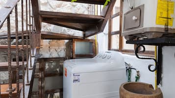 Une cuisine rustique équipée d’un lave-linge, d’un évier et d’un tabouret en bois.