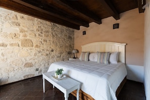 A bedroom with a stone wall, a wooden ceiling, a bed with white bedding, and a small table with a plant. - Casa La Virgen | Washing machine + Parking (Heroica Puebla de Zaragoza)