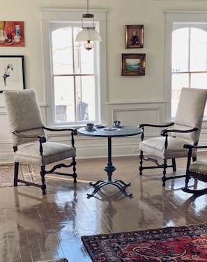 A room with two upholstered chairs, a round table, a hanging light fixture, and a large window.