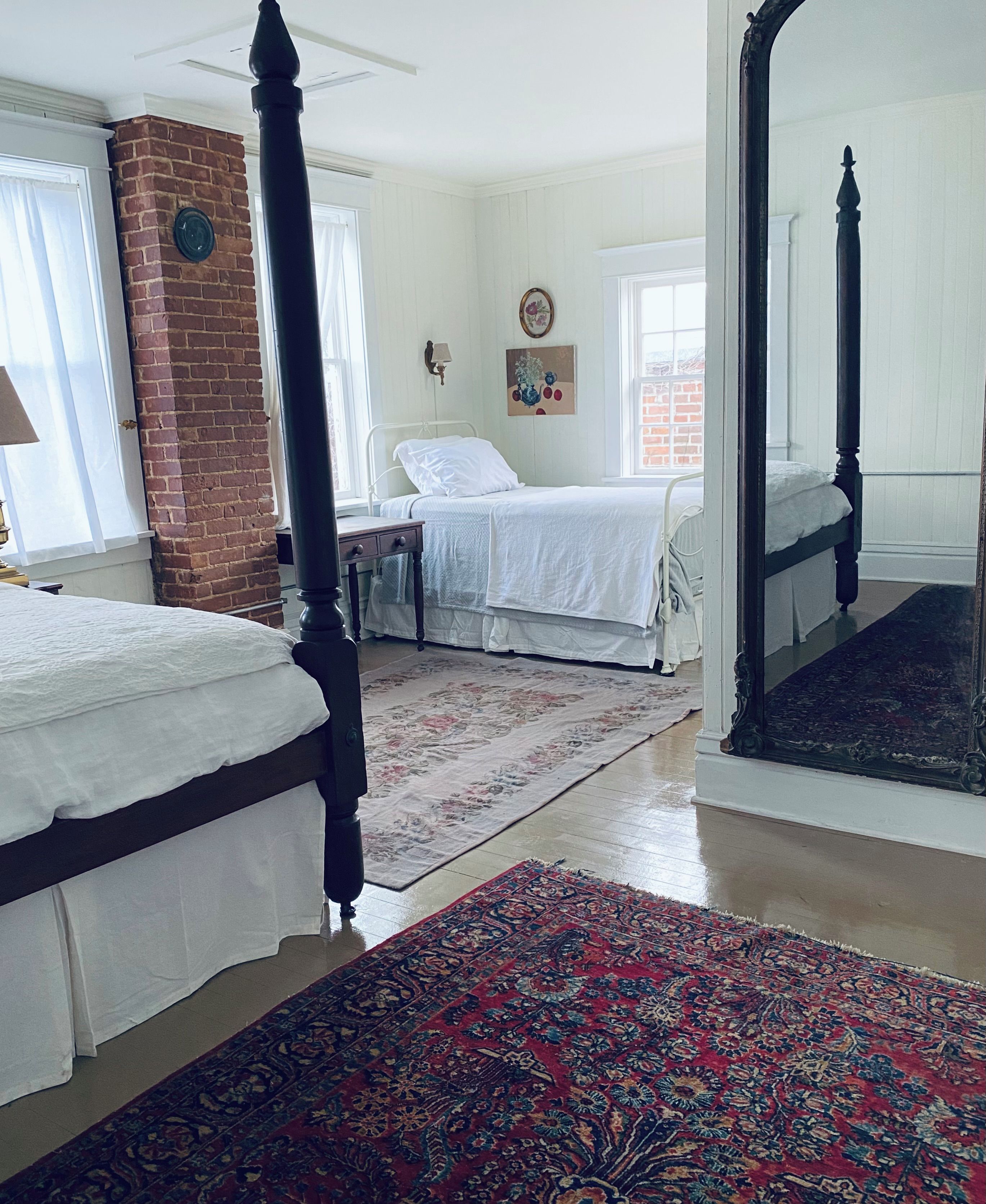 A bedroom with two beds, a large mirror, a brick wall, and a window.