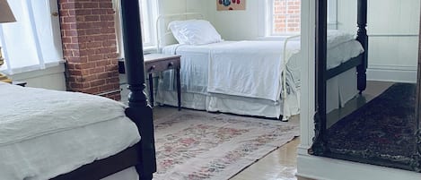 A bedroom with two beds, a large mirror, a brick wall, and a window.