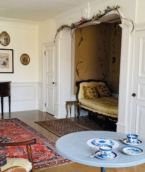 Um quarto com cama, uma mesa redonda com pratos azuis e brancos, um tapete com padrão vermelho e uma pequena mesa com uma cadeira.