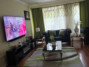 Sala de estar com televisão de tela plana, sofá escuro, mesa de centro e cortina verde.