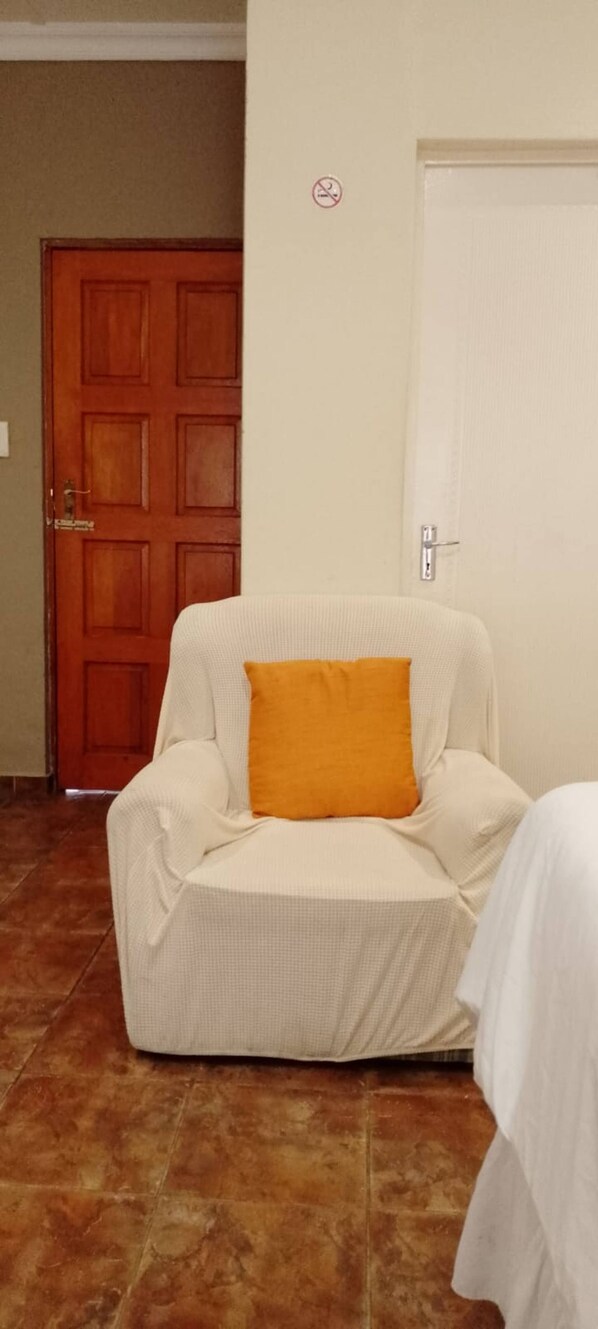 A hotel room with a white armchair, a wooden door, and a white wall. - Room-alexandra Bed & Breakfast Room 5 (Pietermaritzburg)